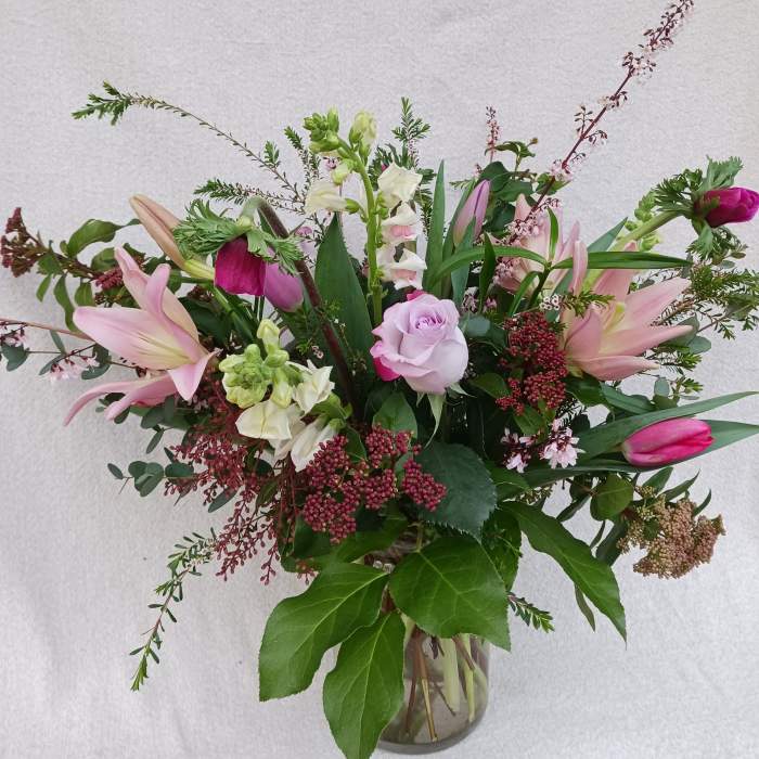 Tall arrangement of pink lilies, tulips, and a lavender rose in a clear glass vase
