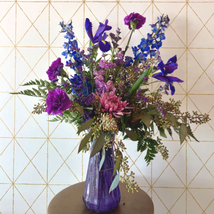 Purple and blue mixed flower arrangement in a tall purple vase