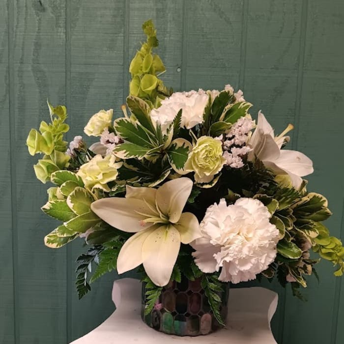 White lilies and carnations in a decorative vase with green foliage