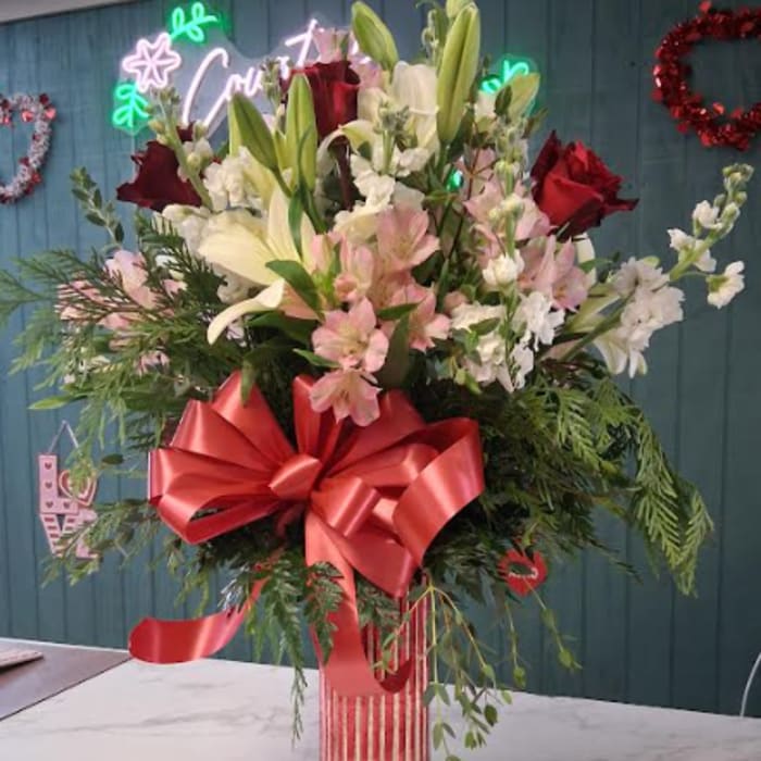 Tall bouquet of lilies, roses, and pink flowers in a striped vase with a red bow