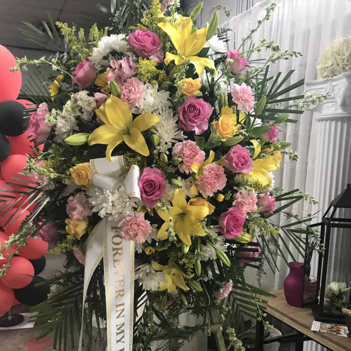 Large standing floral spray with pink and yellow flowers and a memorial ribbon