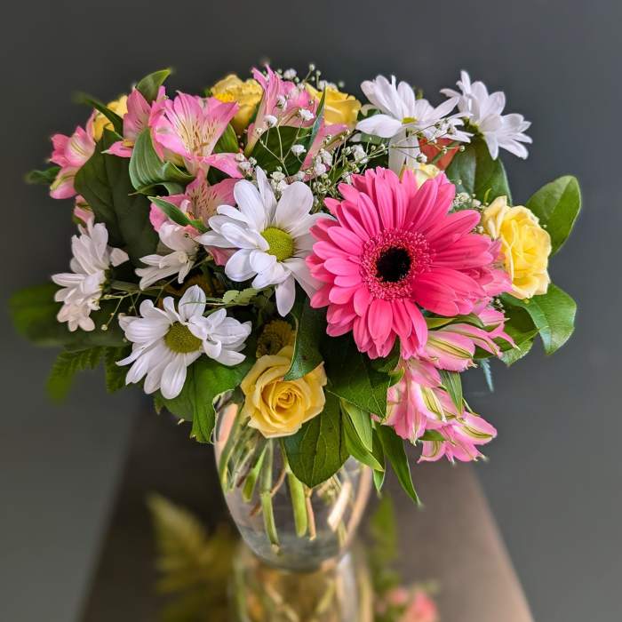 Mixed bouquet of pink gerbera, white daisies, yellow roses, and pink alstroemeria in a clear glass vase