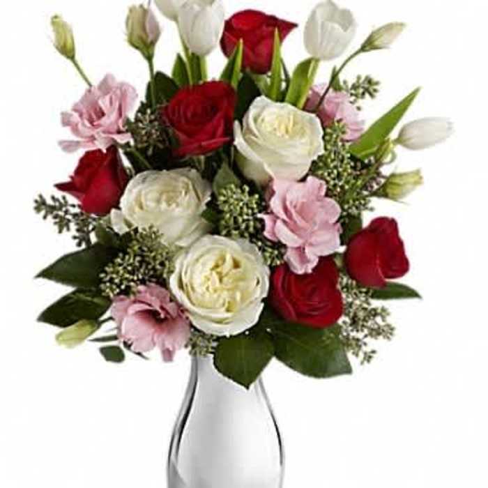 Arrangement of red and white roses, pink blooms, and white tulips in a shiny silver vase