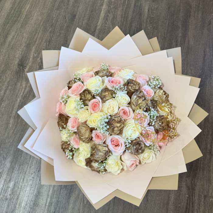 Round bouquet of pink, cream, and brown roses wrapped in layered paper