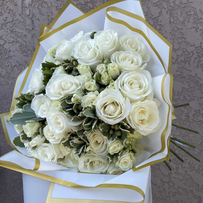 Bouquet of white roses wrapped in white paper with gold trim