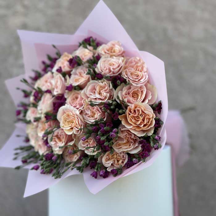 Bouquet of pale pink roses with purple filler flowers in pink wrapping