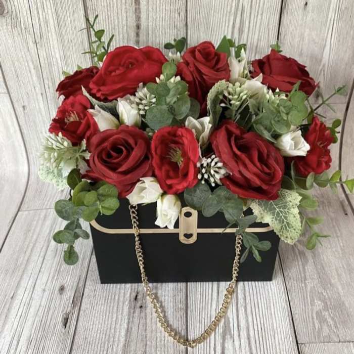 Red roses and white blooms arranged in a black box with a gold chain handle.