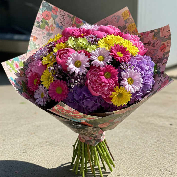 Mixed bouquet of pink, purple, and yellow flowers wrapped in patterned paper