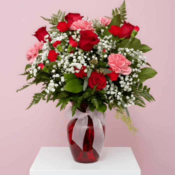 Red roses and pink carnations in a red glass vase with a white ribbon