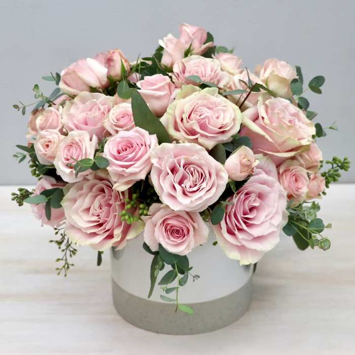 Pink roses arranged in a round white vase with eucalyptus accents