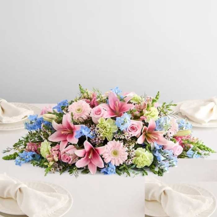 Low floral centerpiece with pink lilies, roses, and blue accents on a white table