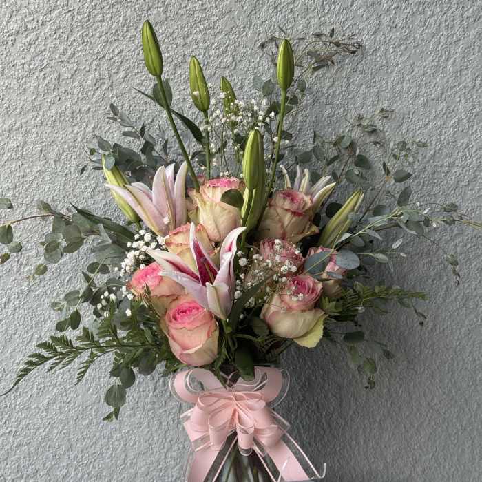 Pink roses and lilies in a glass vase with a pink ribbon
