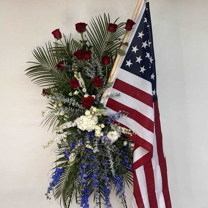 Standing floral spray with red, white, and blue flowers beside an American flag