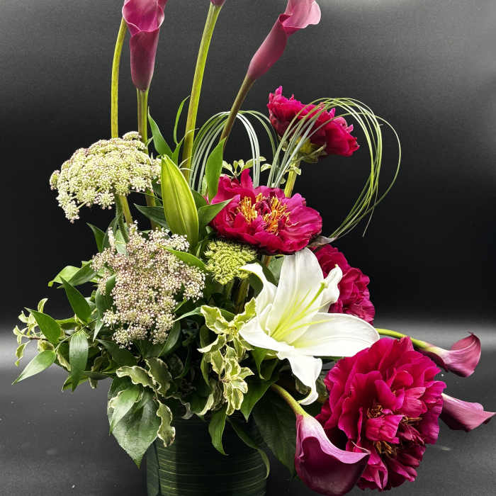 Magenta calla lilies and pink blooms in a glass vase