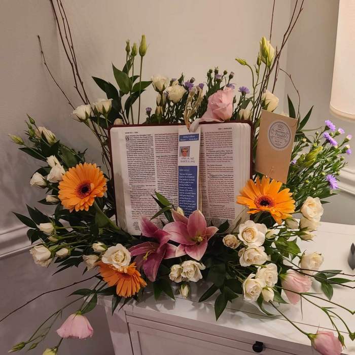 Floral sympathy arrangement around an open book with orange gerberas and pink lilies