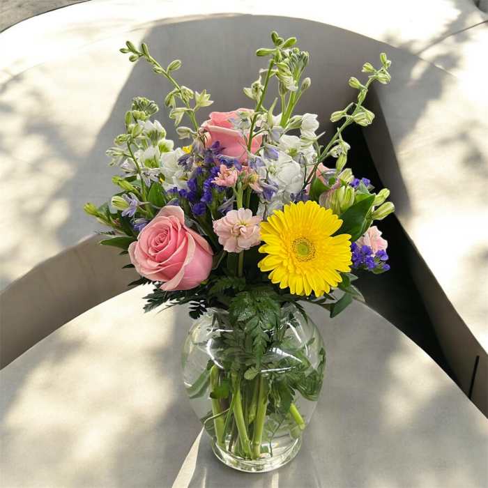 Mixed bouquet of pink roses, yellow gerbera daisy, and pastel flowers in a clear glass vase