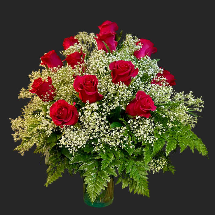 Red roses arranged with white filler flowers in a glass vase