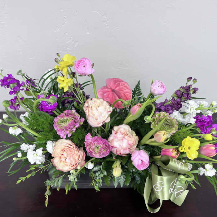 Low floral arrangement with pink, purple, yellow, and white blooms in a rectangular container