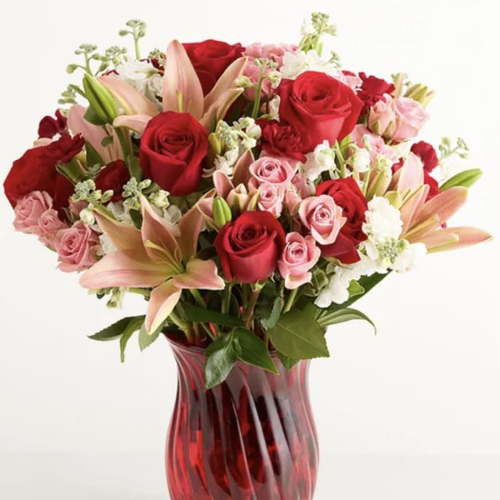 Red and pink roses with lilies in a red glass vase
