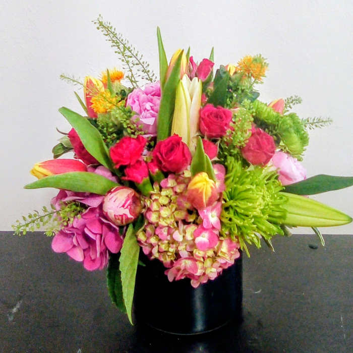 Colorful mixed bouquet with pink hydrangeas, red roses, tulips, and lilies in a black cylinder vase