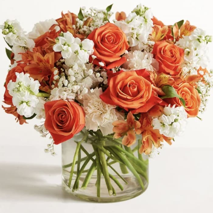 Orange roses and white flowers arranged in a clear glass vase