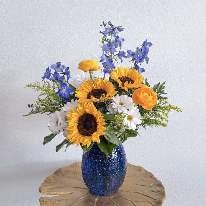 Bouquet of sunflowers, blue delphinium, and white daisies in a blue vase
