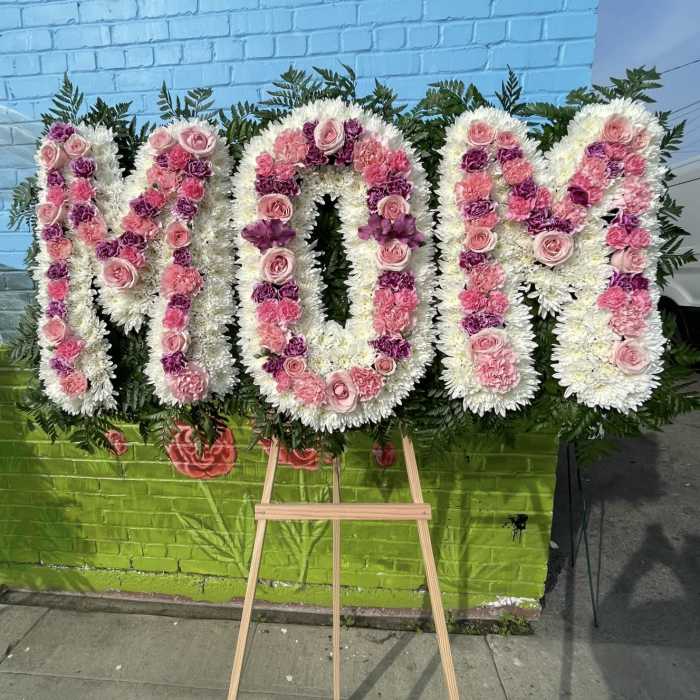 Large floral standing tribute spelling "MOM" in pink and white flowers