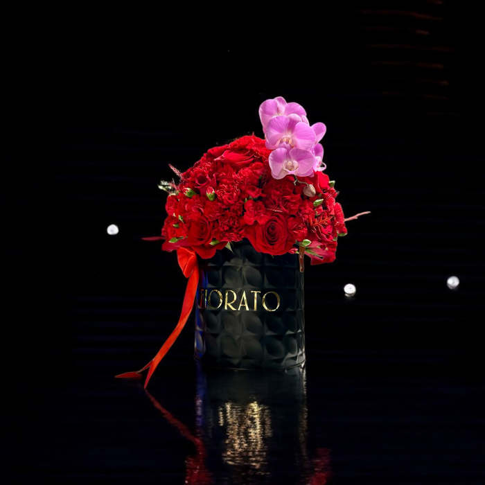 Red rose arrangement in a black container with pink orchids