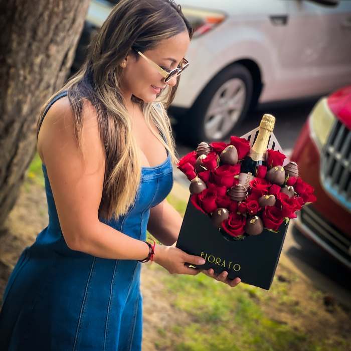 Woman holding a box of red roses and chocolates with a champagne bottle