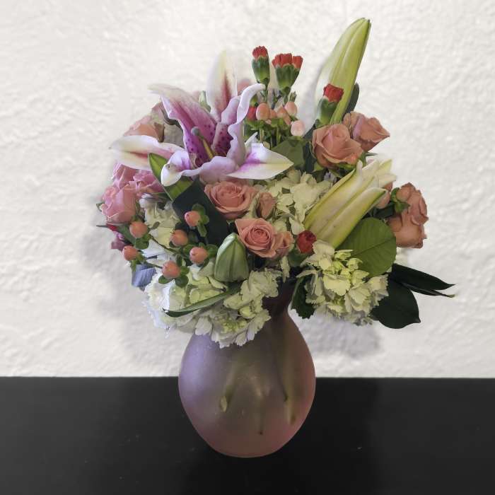 Pink and white lilies, roses, and carnations arranged in a frosted pink glass vase.