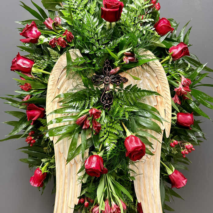 Standing floral spray with red roses and a wooden angel-wing cross