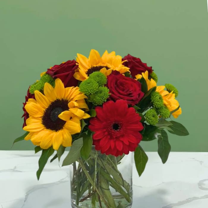 Bouquet of sunflowers, red roses, and a red gerbera daisy in a glass vase