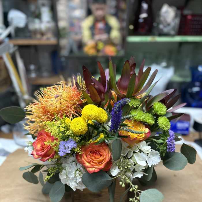 Mixed bouquet with orange roses, yellow mums, and white hydrangea in a low container