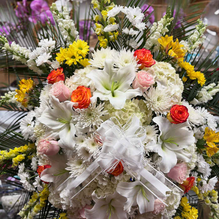 Large white floral spray with lilies, roses, and daisies tied with a white ribbon