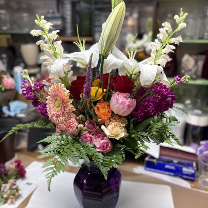 Mixed bouquet with lilies, roses, and purple blooms in a dark vase