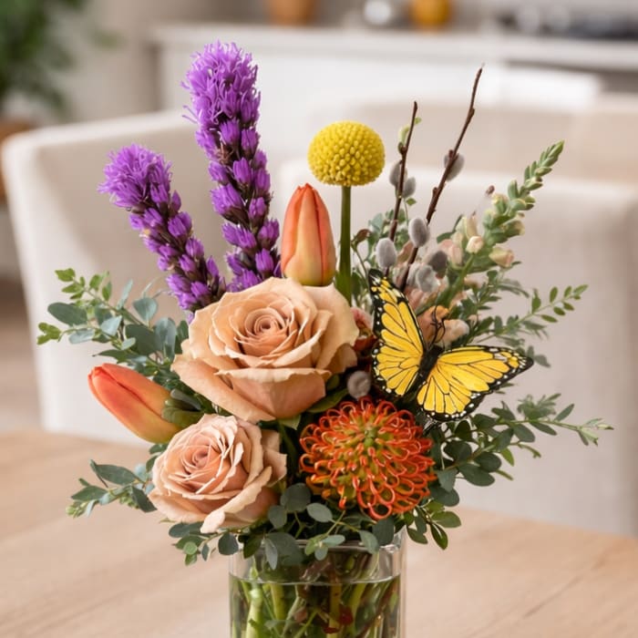 Mixed bouquet in a clear glass vase with roses, tulips, and a butterfly accent