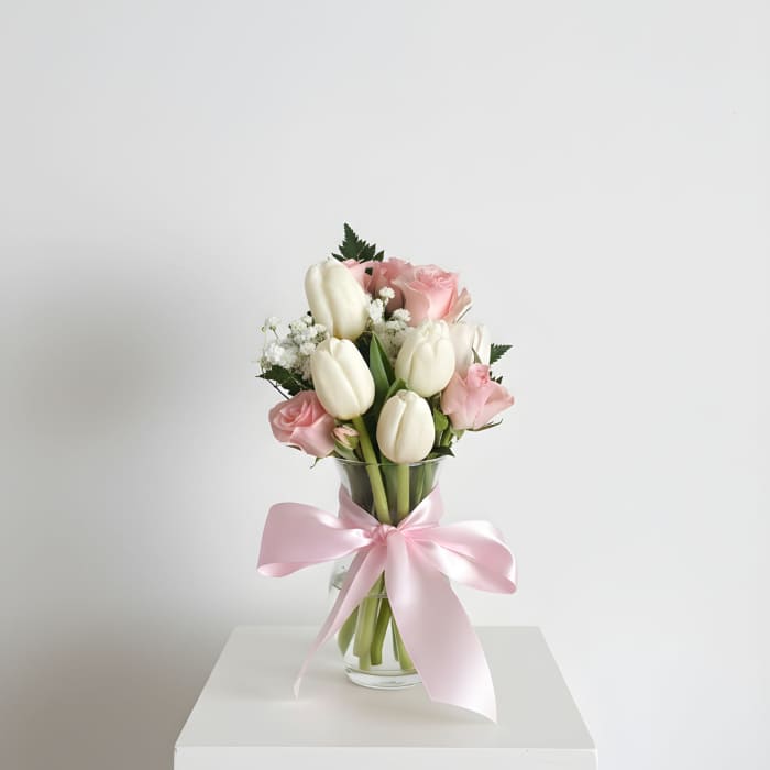 Pink roses and white tulips in a glass vase with a pink ribbon