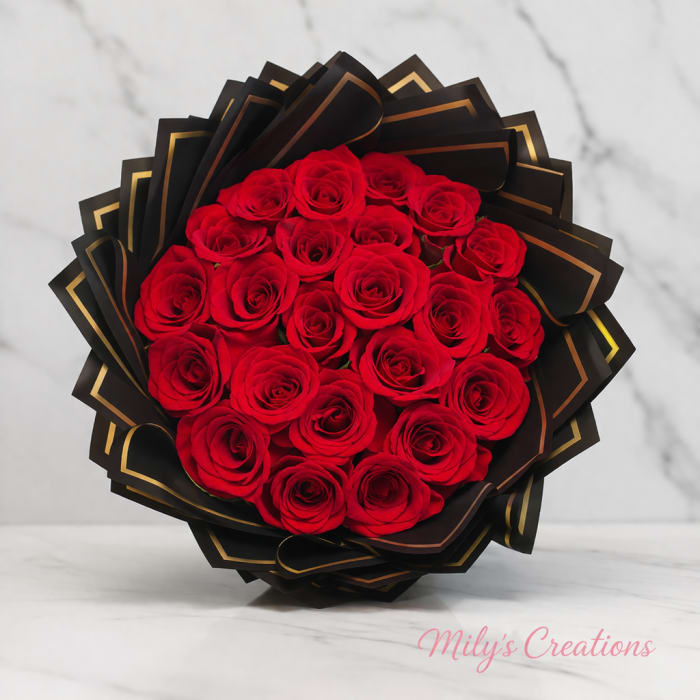 Round bouquet of red roses wrapped in black and gold paper on a marble surface