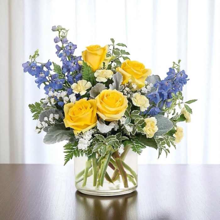 Yellow roses and blue delphinium in a clear glass vase