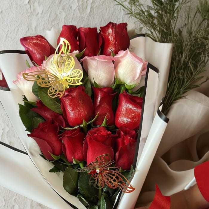 Bouquet of red and pale pink roses wrapped in white paper with a red bow