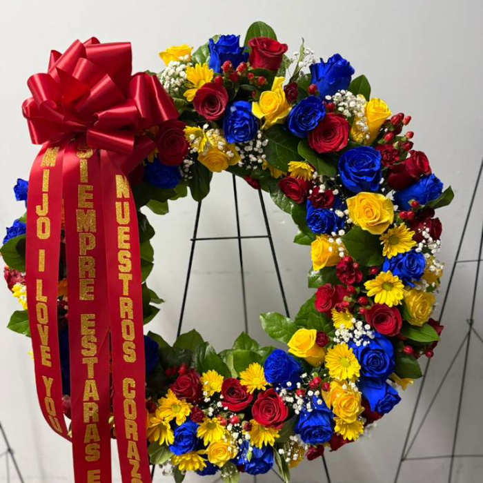 Circular floral wreath with red, blue, and yellow roses and a large red bow