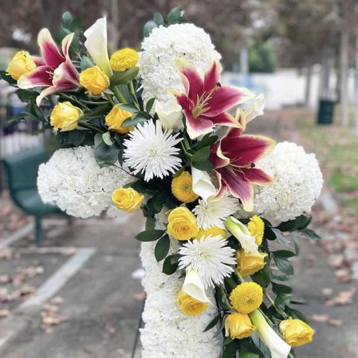 Cross-shaped floral arrangement with white blooms, yellow roses, and burgundy lilies