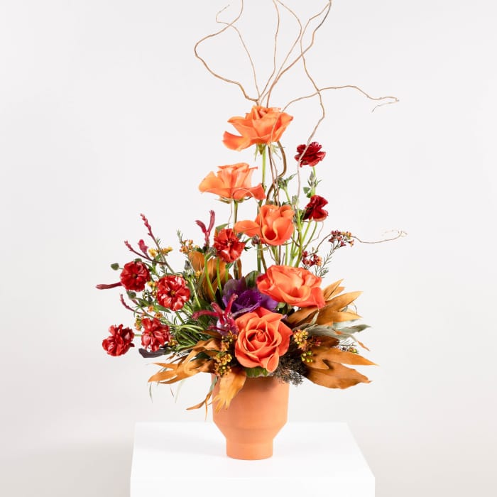 Orange and red floral arrangement in a terracotta vase with tall branches