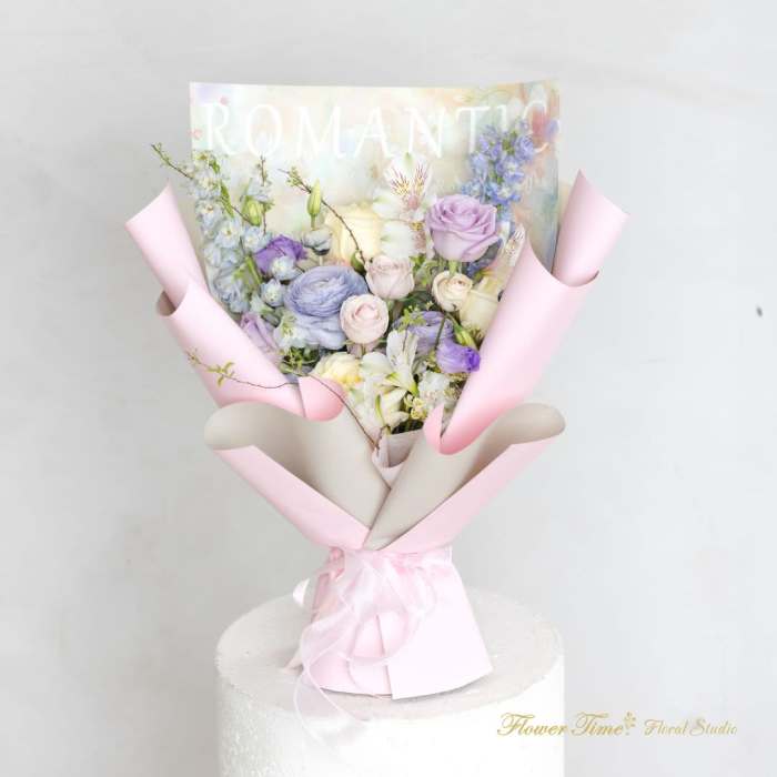 Pastel bouquet of roses, lilies, and blue flowers wrapped in pink paper