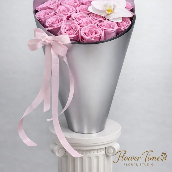Pink roses in a silver cone wrap with a white orchid accent and pink ribbon