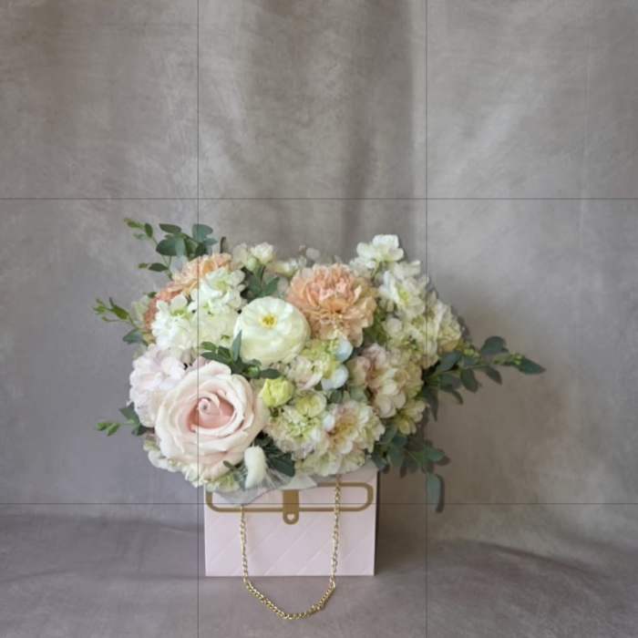 Pastel flower arrangement in a pink gift box with a gold chain handle