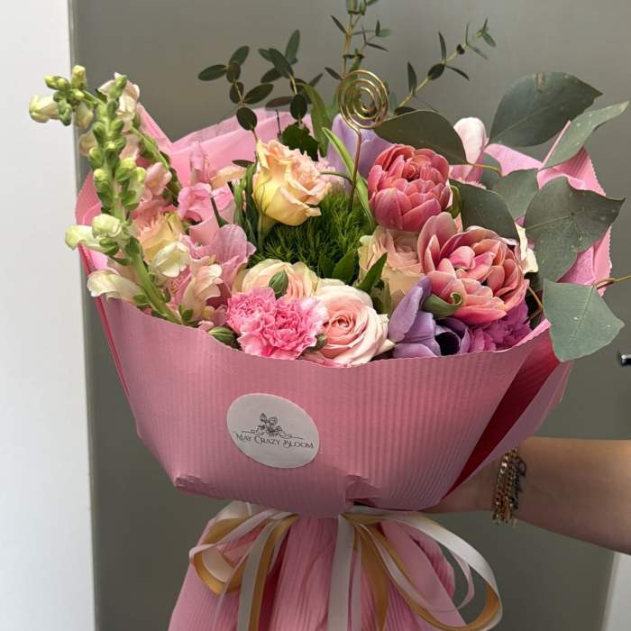 Pink mixed bouquet with roses and purple blooms wrapped in pink paper