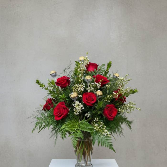 Red roses arranged in a clear glass vase with greenery and small white filler flowers