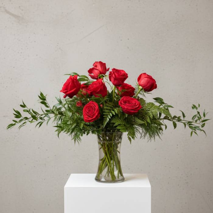 Red roses arranged in a clear glass vase with greenery