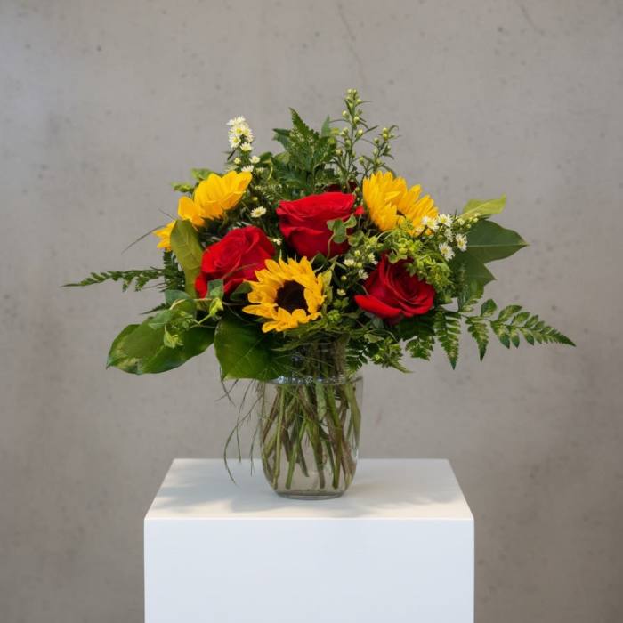 Bouquet of red roses and yellow sunflowers in a clear glass vase